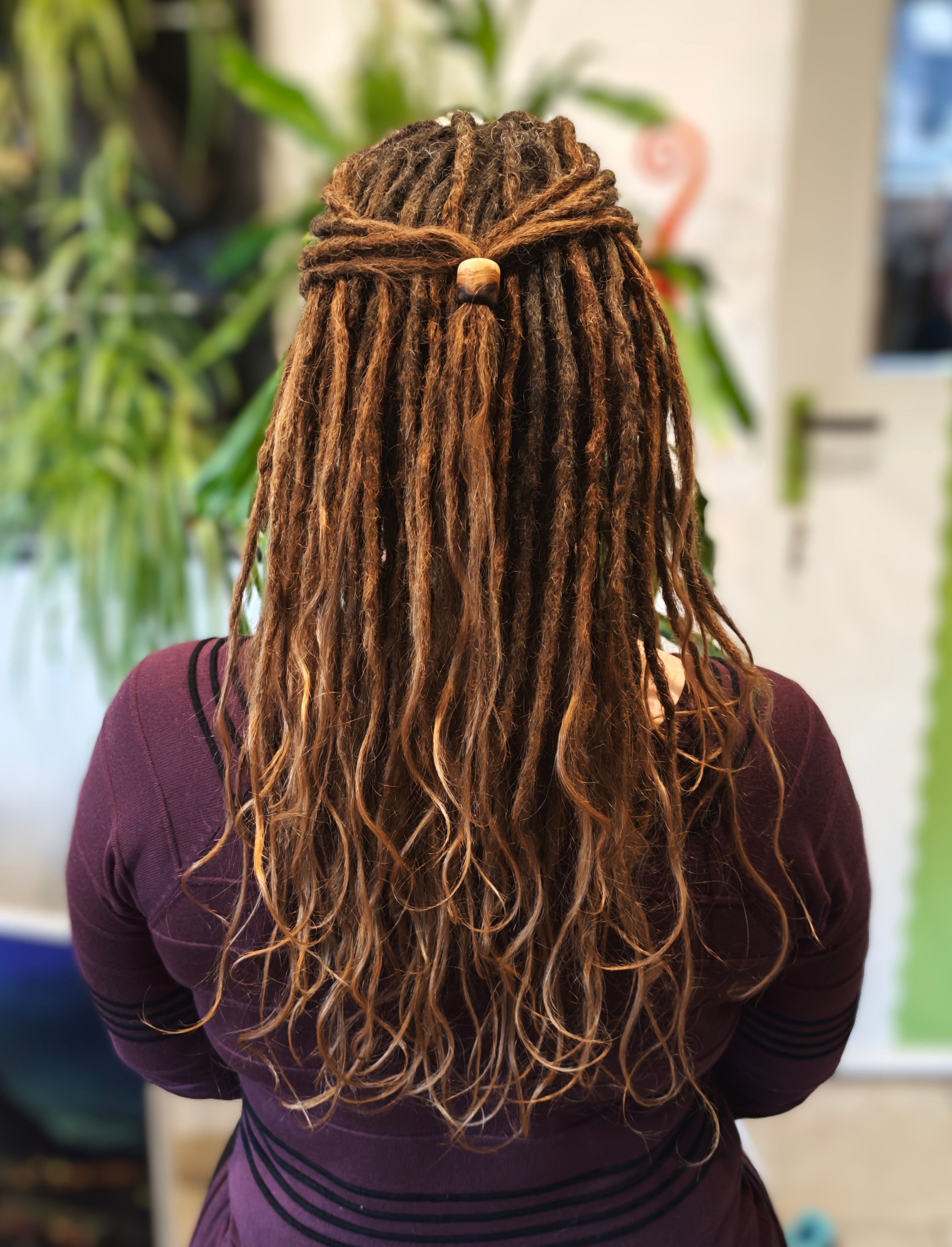 Frau mit langen Dreads mit lockige offenen Enden und einer Baumperlen mit großem Durchmesser die als Haargummi benutzt wird
